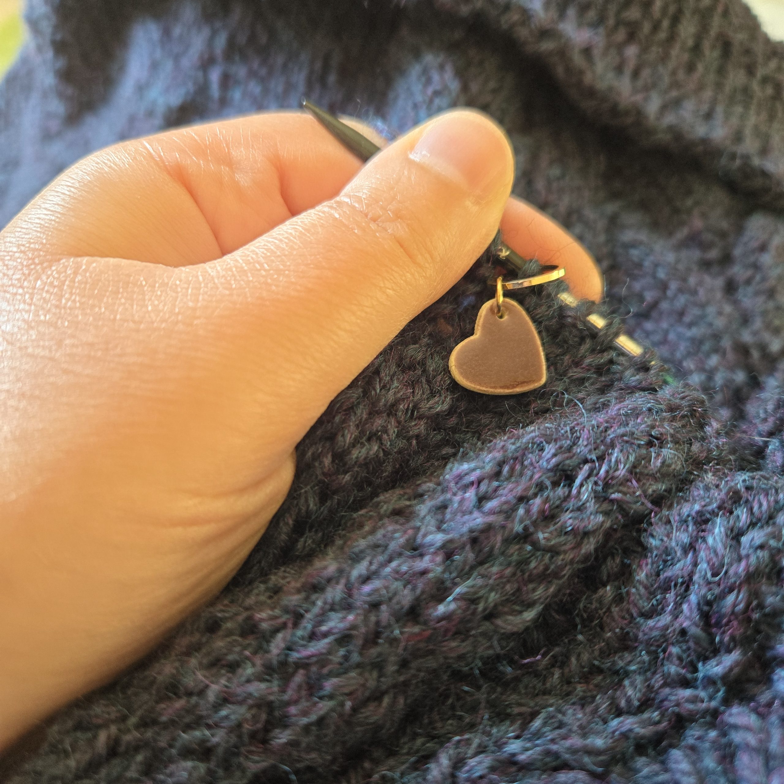 Main qui tient une aiguille de tricot circulaire, marqueur de maille cœur, gilet tricoté