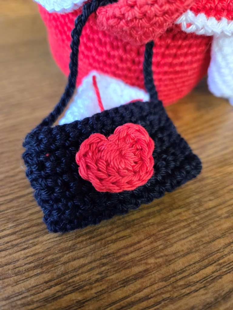 Enveloppe en crochet noir, avec un cœur rouge dessus et une lettre qui dépasse.