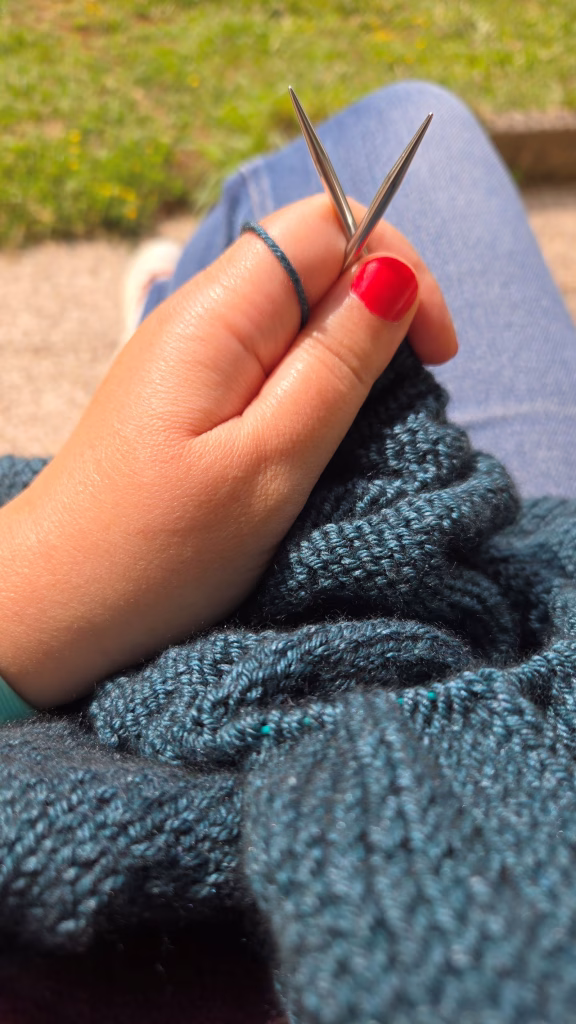 Main qui tient un tricot en cours dehors au soleil.
