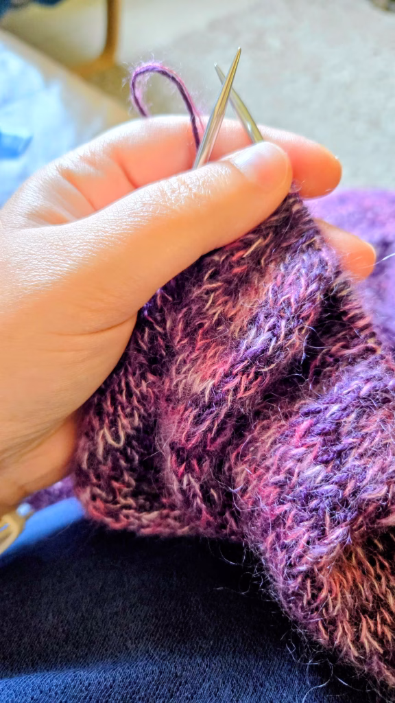 Mains qui tiennent le tricot en cours.